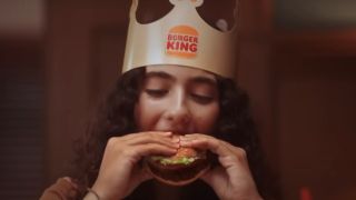 A woman eats a Whopper with a Burger King crown on.